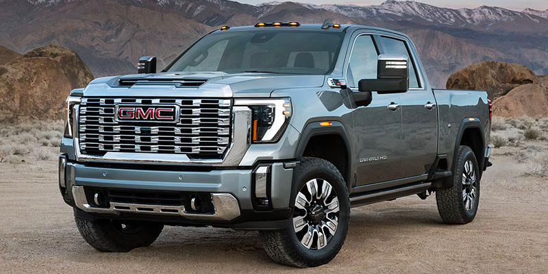 A silver 2025 GMC Sierra HD parked on rugged terrain with an arid landscape behind