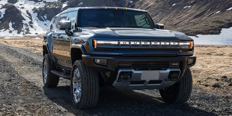 Black GMC Hummer EV SUV on a rocky mountain road with snow-capped hills in the background.