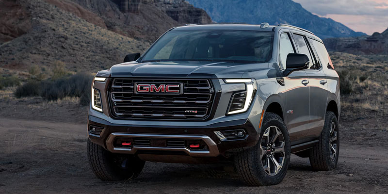 Gray GMC SUV parked on a rugged desert landscape with mountains in the background.