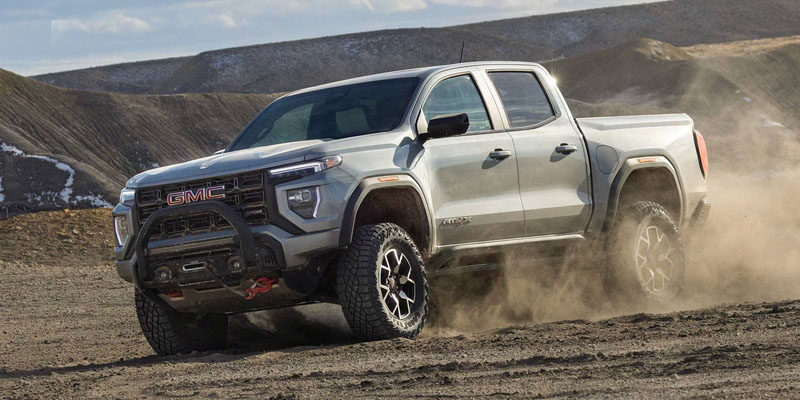 GMC pickup truck driving off-road on dirt terrain, kicking up dust in a rugged landscape.