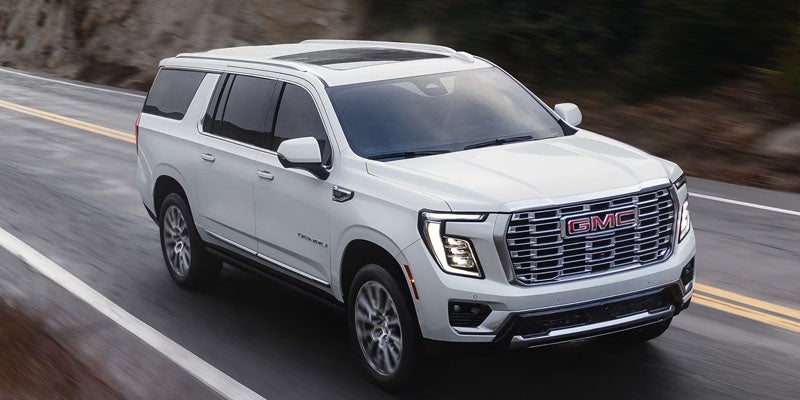 2026 GMC Yukon driving on the road, showcasing its sleek white exterior and modern design.
