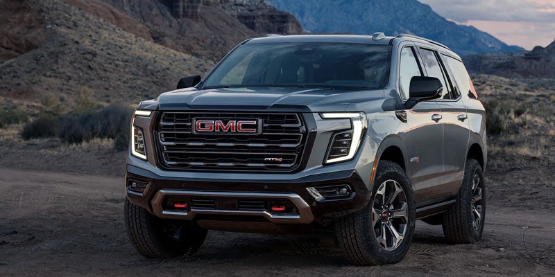 Front view of the 2026 GMC Yukon AT4 with a bold grille and rugged design in a mountainous landscape.