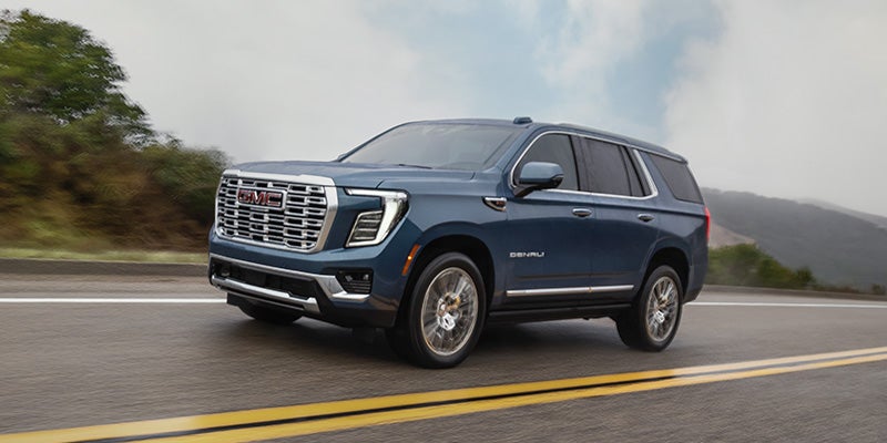 2026 GMC Yukon driving on the road, highlighting its striking blue exterior and refined design.